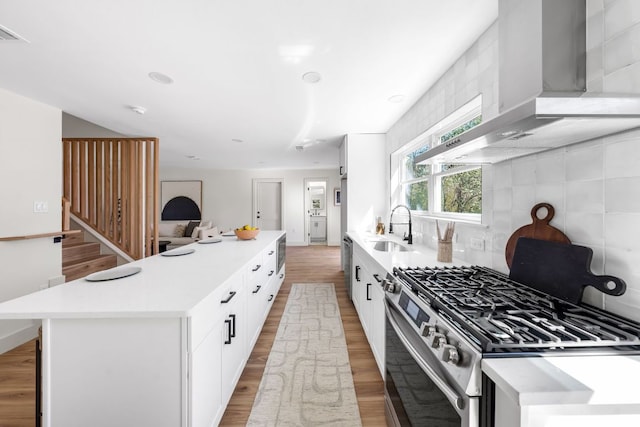 kitchen with wall chimney range hood, stainless steel range with gas cooktop, light wood-style floors, and a sink