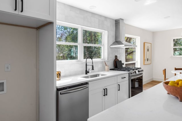 kitchen with stainless steel appliances, a sink, light countertops, wall chimney range hood, and tasteful backsplash