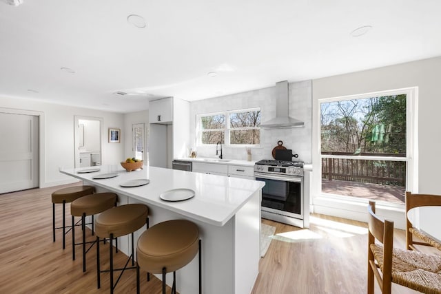 kitchen featuring wall chimney exhaust hood, a kitchen breakfast bar, light countertops, stainless steel appliances, and a sink