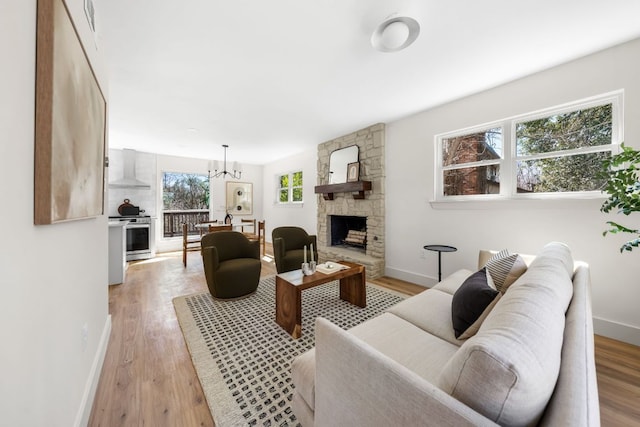 living area with light wood-style flooring, a fireplace, baseboards, and a notable chandelier