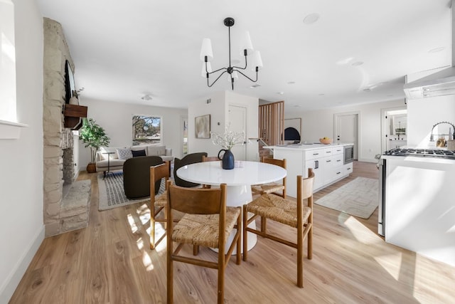 dining room featuring light wood-style flooring, a fireplace, baseboards, and a notable chandelier