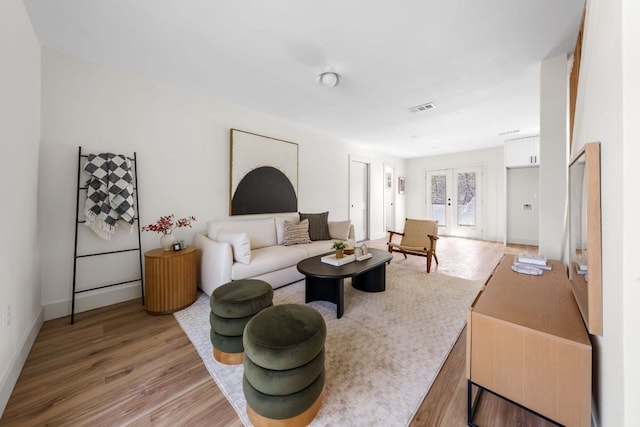 living room featuring light wood-type flooring, visible vents, and baseboards