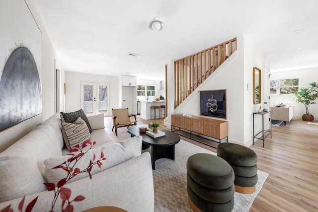 living room featuring french doors, stairway, wood finished floors, and a healthy amount of sunlight