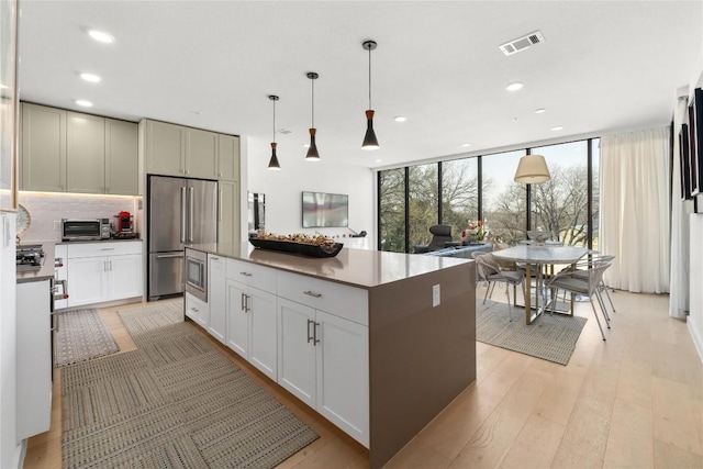 kitchen featuring light wood finished floors, visible vents, appliances with stainless steel finishes, a center island, and backsplash