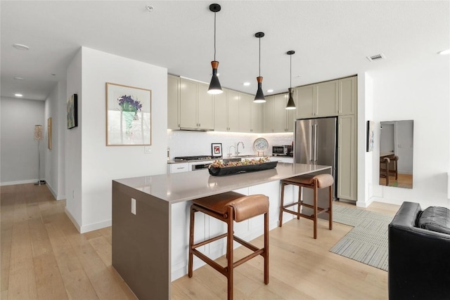 kitchen with a kitchen island, visible vents, a kitchen breakfast bar, decorative backsplash, and light wood finished floors