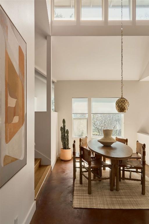 dining space with a healthy amount of sunlight, concrete floors, baseboards, and a towering ceiling