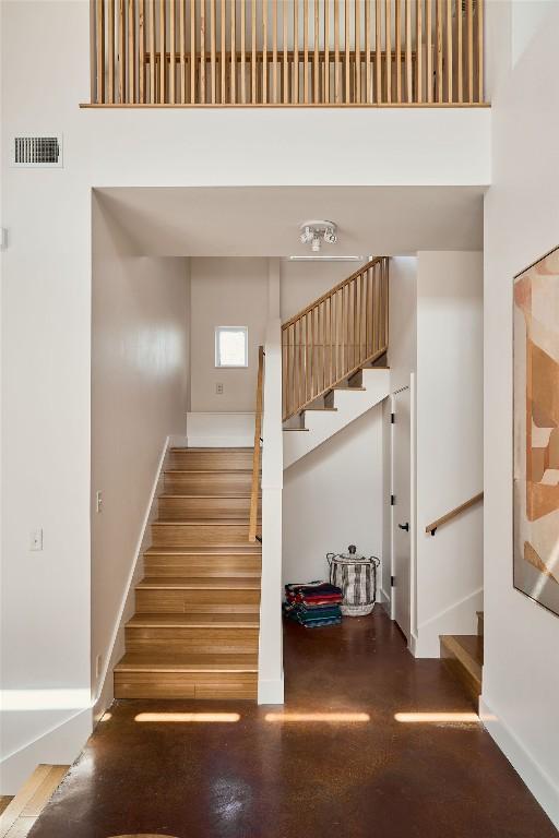 stairs featuring wood finished floors, a towering ceiling, visible vents, and baseboards