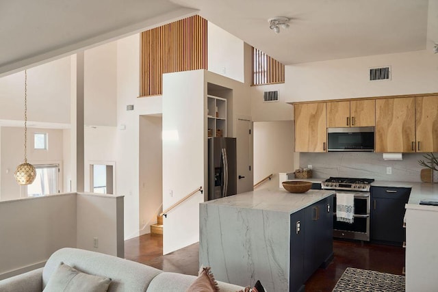 kitchen with a high ceiling, visible vents, stainless steel appliances, and a center island