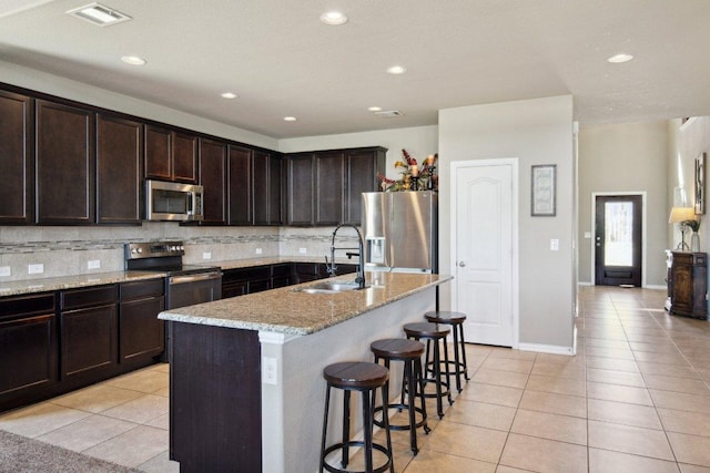 1010 Papaya Cv, Hutto, TX 78634 - kitchen featuring stainless steel appliances, light tile patterned floors, decorative backsplash, a kitchen breakfast bar, and dark brown cabinets