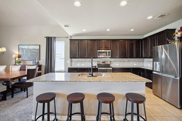 kitchen featuring dark brown cabinetry, stainless steel appliances, visible vents, decorative backsplash, and light stone countertops