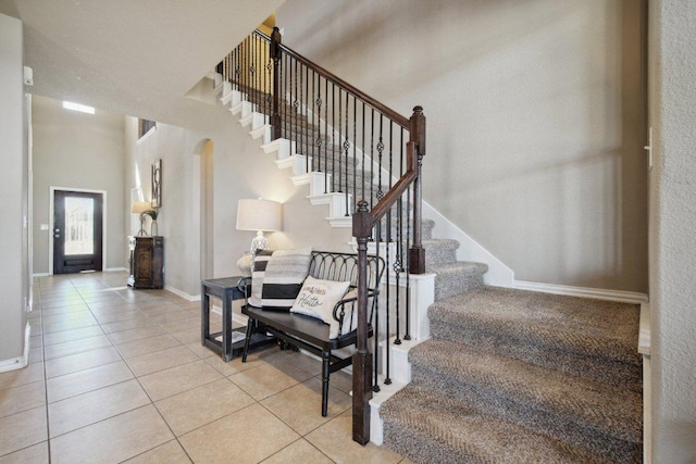 staircase with arched walkways, baseboards, a high ceiling, and tile patterned floors