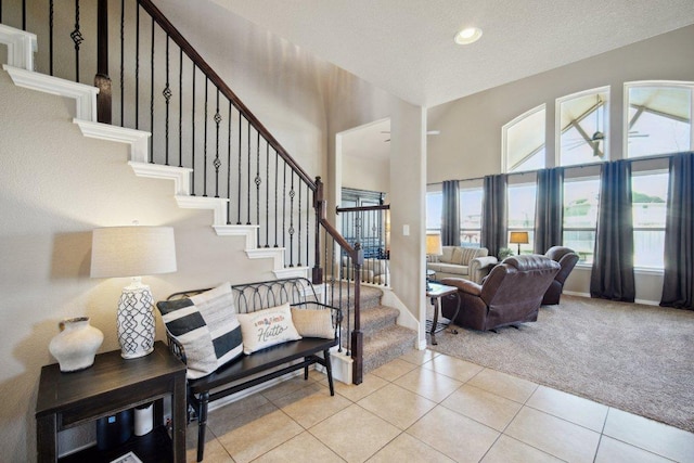 interior space featuring light colored carpet, a high ceiling, light tile patterned flooring, baseboards, and stairs