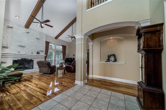 entryway with light tile patterned floors, high vaulted ceiling, a stone fireplace, a ceiling fan, and beamed ceiling