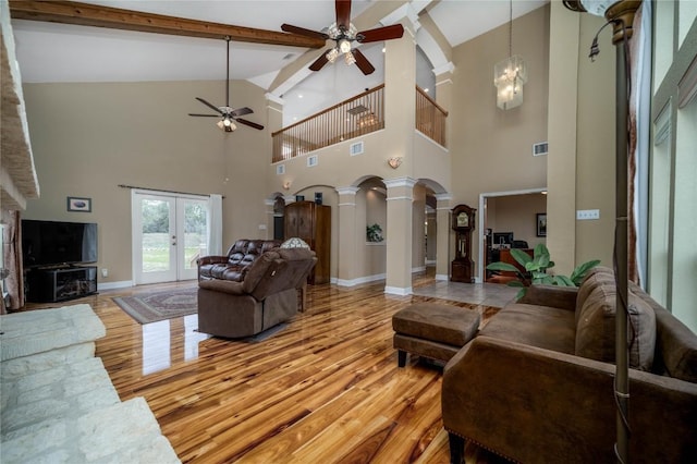 living room featuring decorative columns, baseboards, french doors, light wood-style floors, and ceiling fan with notable chandelier