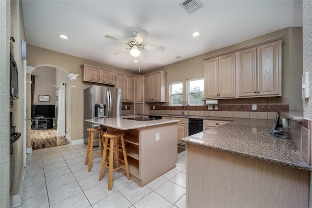 kitchen featuring arched walkways, a breakfast bar area, a kitchen island, visible vents, and stainless steel fridge with ice dispenser