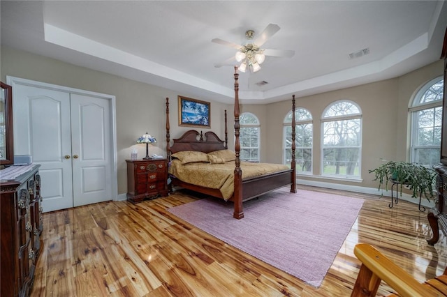 bedroom with visible vents, a tray ceiling, light wood-style flooring, and baseboards