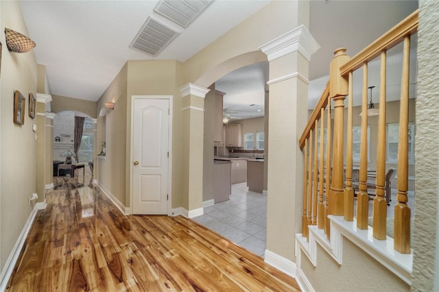 corridor featuring light wood-type flooring, ornate columns, visible vents, and arched walkways