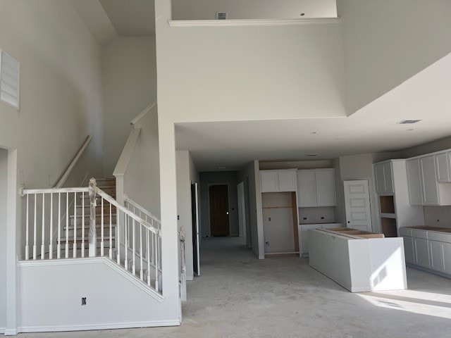 kitchen with a towering ceiling, unfinished concrete floors, white cabinetry, and a center island