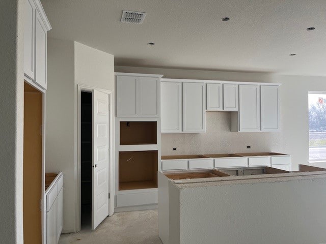 kitchen with unfinished concrete floors, visible vents, a textured ceiling, and a center island