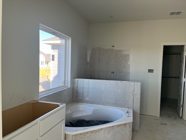 bathroom with concrete flooring, a spacious closet, a garden tub, and visible vents