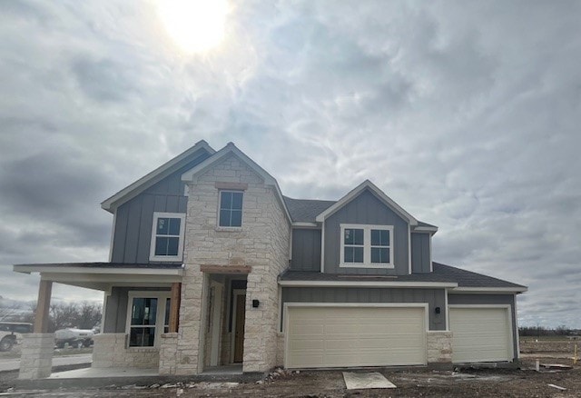 view of front of property with an attached garage, stone siding, board and batten siding, and roof with shingles