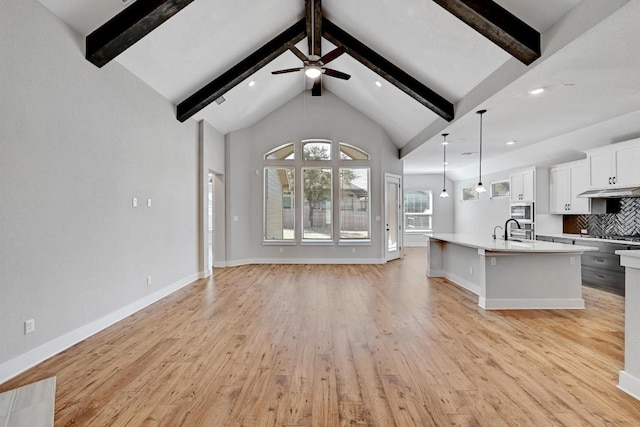 unfurnished living room with beamed ceiling, baseboards, light wood-style floors, and a sink