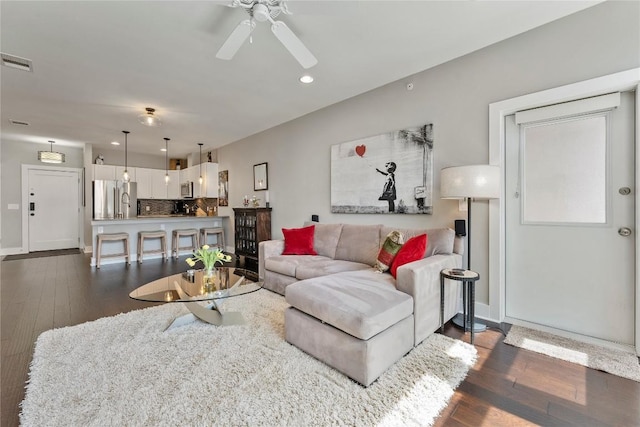 living area with dark wood-type flooring, visible vents, baseboards, and a ceiling fan