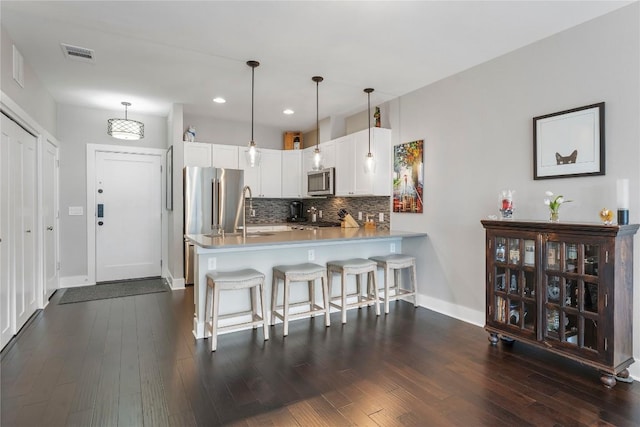 kitchen featuring a peninsula, visible vents, appliances with stainless steel finishes, tasteful backsplash, and dark wood finished floors