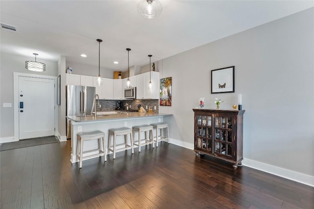 kitchen featuring tasteful backsplash, visible vents, dark wood finished floors, a peninsula, and stainless steel appliances