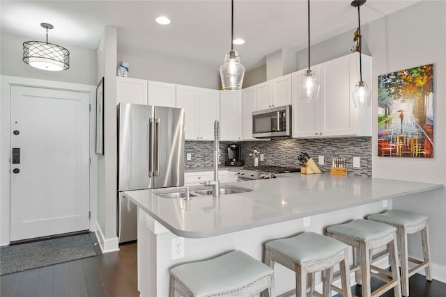 kitchen featuring appliances with stainless steel finishes, backsplash, a peninsula, white cabinetry, and a sink