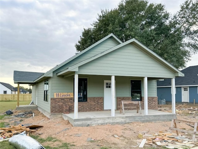 view of front facade with brick siding, a porch, and fence