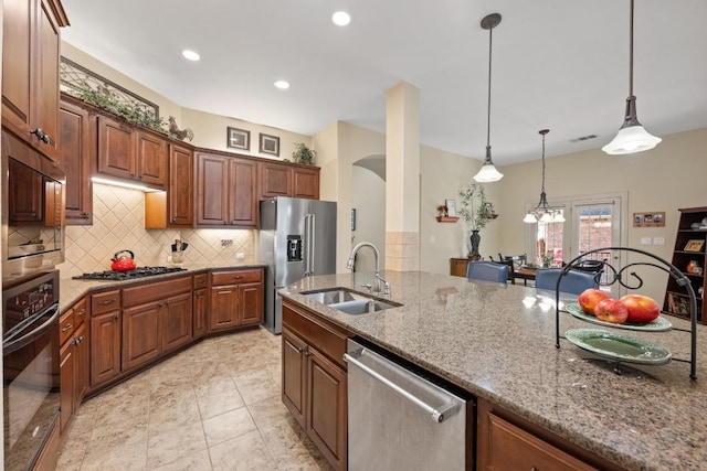 kitchen featuring stainless steel appliances, hanging light fixtures, decorative backsplash, stone countertops, and a sink