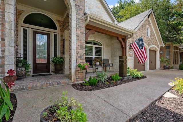 entrance to property featuring brick siding, a porch, an attached garage, stone siding, and driveway