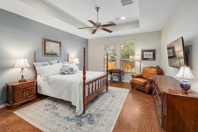 bedroom featuring wood finished floors, a raised ceiling, visible vents, and baseboards