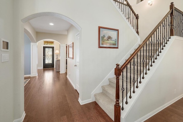 foyer with dark wood-type flooring, a towering ceiling, and baseboards