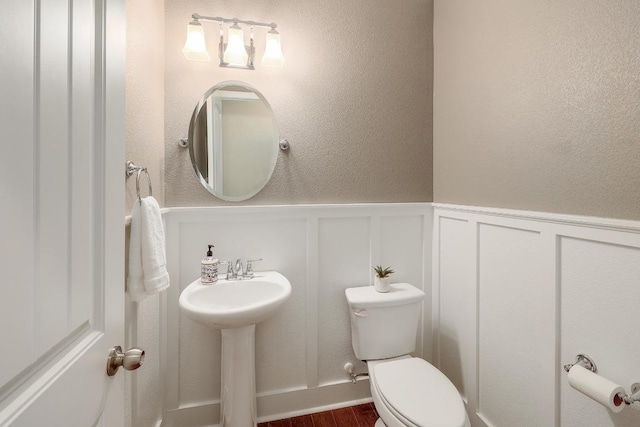 bathroom with a wainscoted wall, a decorative wall, toilet, and wood finished floors