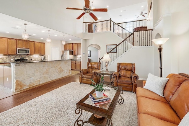 living area featuring arched walkways, recessed lighting, ceiling fan, light wood-type flooring, and stairs