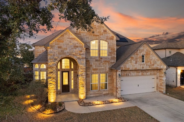 french country home with an attached garage, driveway, roof with shingles, and solar panels