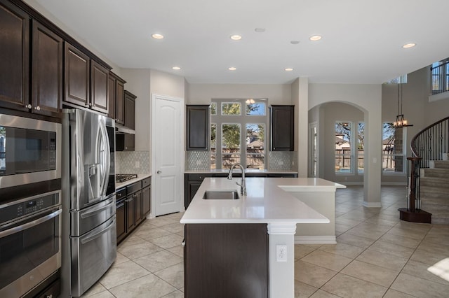 kitchen featuring a sink, light countertops, appliances with stainless steel finishes, decorative backsplash, and a center island with sink