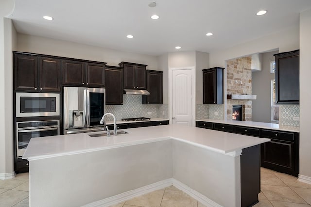 kitchen with under cabinet range hood, a sink, light countertops, appliances with stainless steel finishes, and an island with sink