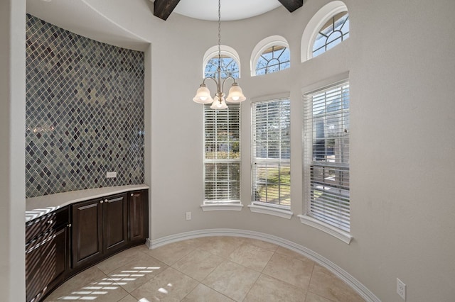 unfurnished dining area featuring baseboards, light tile patterned flooring, a wealth of natural light, and an inviting chandelier