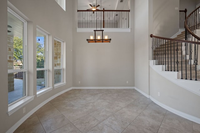 interior space featuring tile patterned floors, a towering ceiling, stairway, baseboards, and ceiling fan with notable chandelier