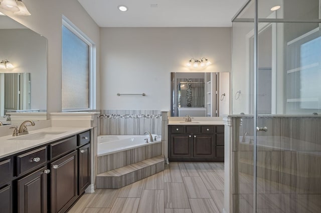 full bath featuring a garden tub, a stall shower, two vanities, and a sink