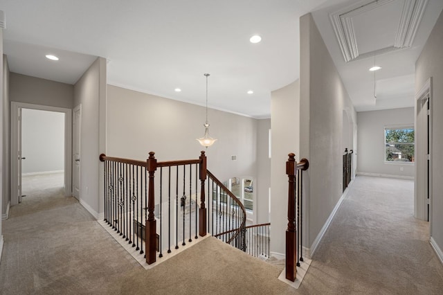 hallway featuring attic access, baseboards, light colored carpet, and an upstairs landing