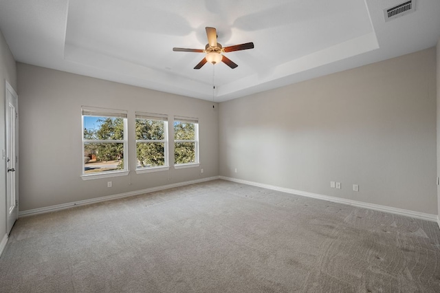 empty room featuring a tray ceiling, carpet flooring, visible vents, and baseboards