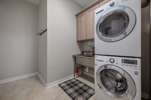 laundry room with stacked washer and dryer, cabinet space, baseboards, and light tile patterned floors