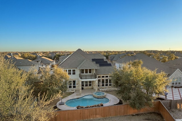 rear view of house with a patio area, a fenced backyard, roof mounted solar panels, and a pool with connected hot tub