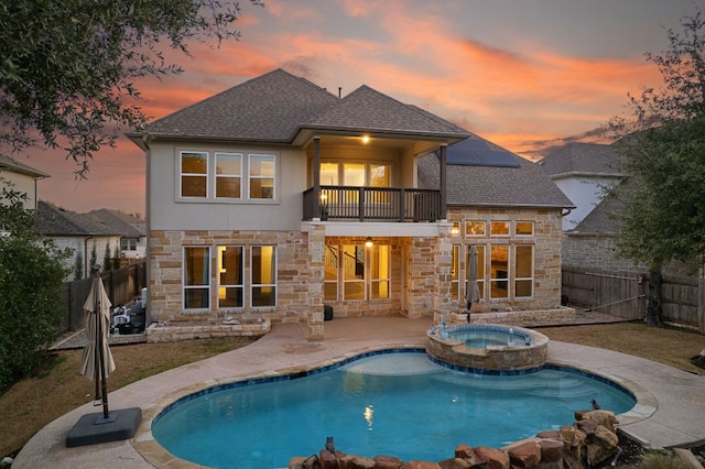 rear view of property with stone siding, a patio area, a fenced backyard, and a balcony