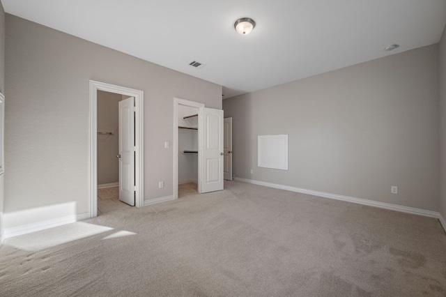 unfurnished bedroom featuring baseboards, visible vents, light colored carpet, a walk in closet, and a closet