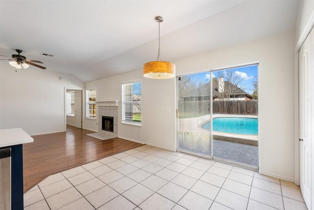 interior space with vaulted ceiling, a tiled fireplace, plenty of natural light, and visible vents